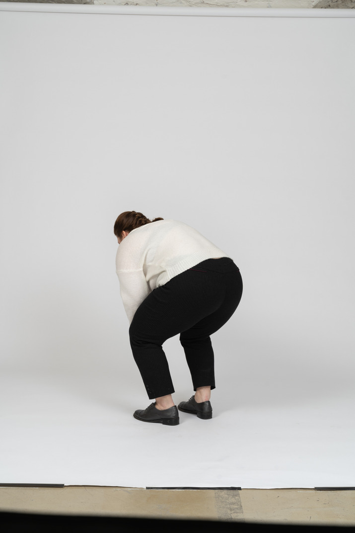 Rear view of a plump woman in casual clothes bending down