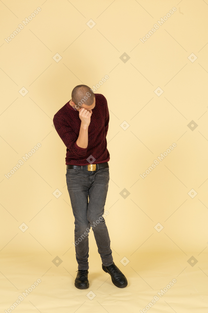 Front view of a depressed young man in red pullover touching his head