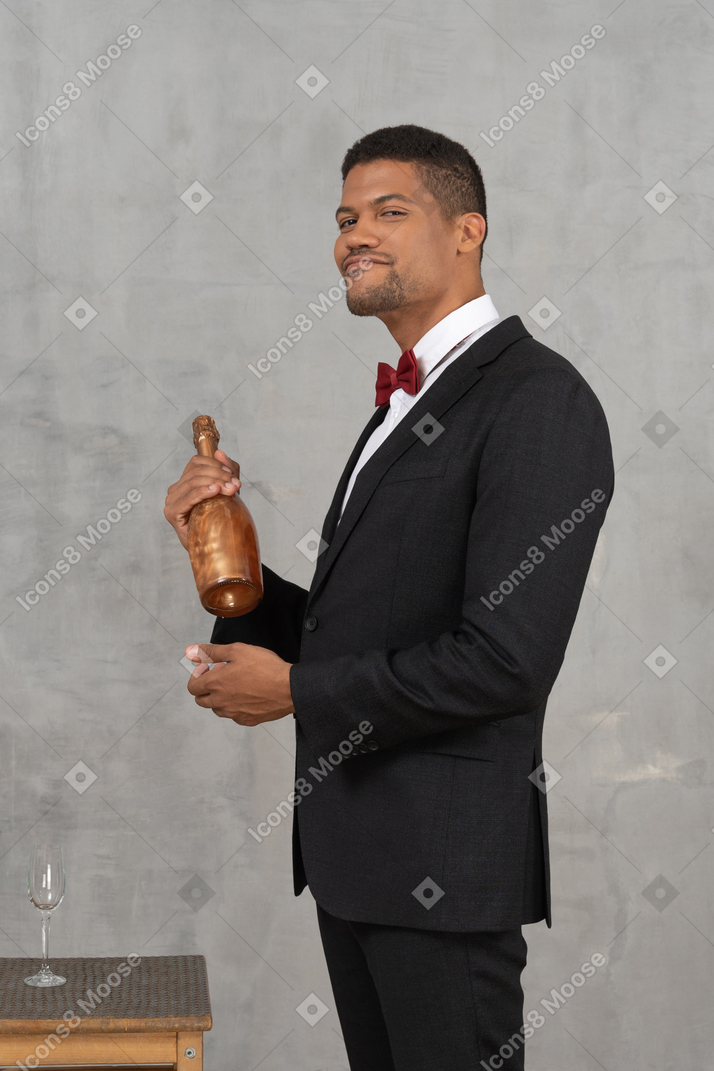 Jeune homme à l'air suffisant, debout avec une bouteille de champagne dans les mains