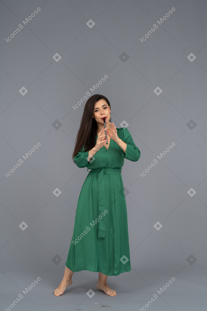 Вид спереди молодой леди в зеленом платье, играющей на флейте