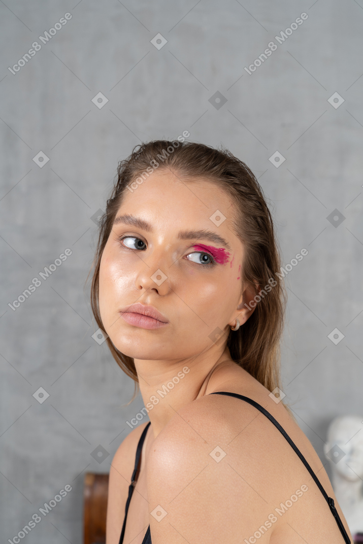 Retrato de una mujer joven con maquillaje de ojos audaz mirando detrás de ella