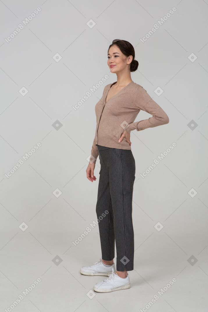 Three-quarter view of a pleased female in pullover and pants putting hand on hip