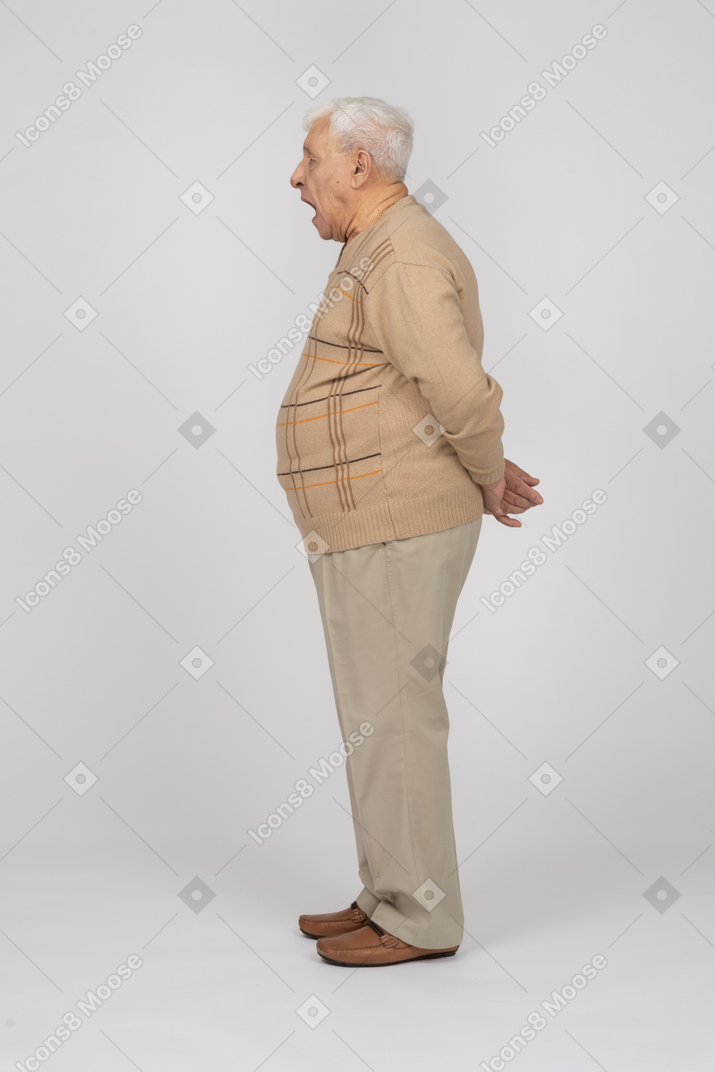 一位身穿休闲服、双手背在身后站立的老人的侧视图