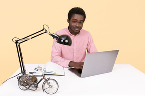 Beau jeune homme assis à la table et à l'aide d'un ordinateur portable