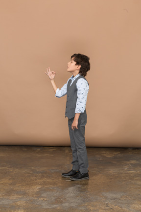 Vista lateral de um menino de terno cinza mostrando sinal de ok