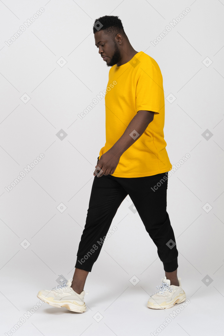 Vista di tre quarti di un giovane uomo dalla pelle scura che cammina con una maglietta gialla