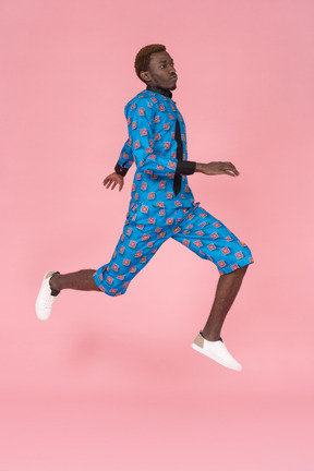 Black man in blue pajamas jumping on pink background