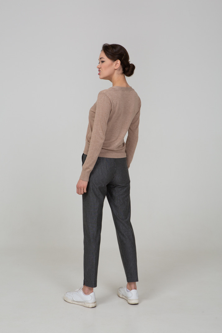 Three-quarter back view of a displeased lady in pullover and pants looking aside
