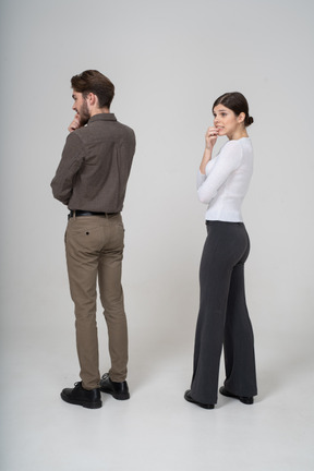 Vista posterior de tres cuartos de una joven pareja nerviosa en ropa de oficina tocando la barbilla
