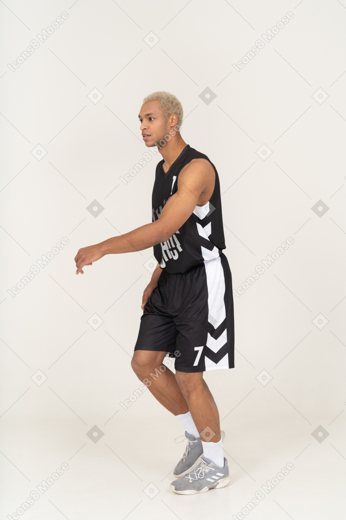 Dreiviertelansicht eines gehenden jungen männlichen basketballspielers, der die hand hebt