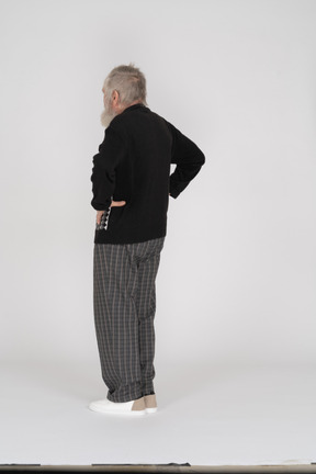 Side view of an elderly man standing with his hands on his hips