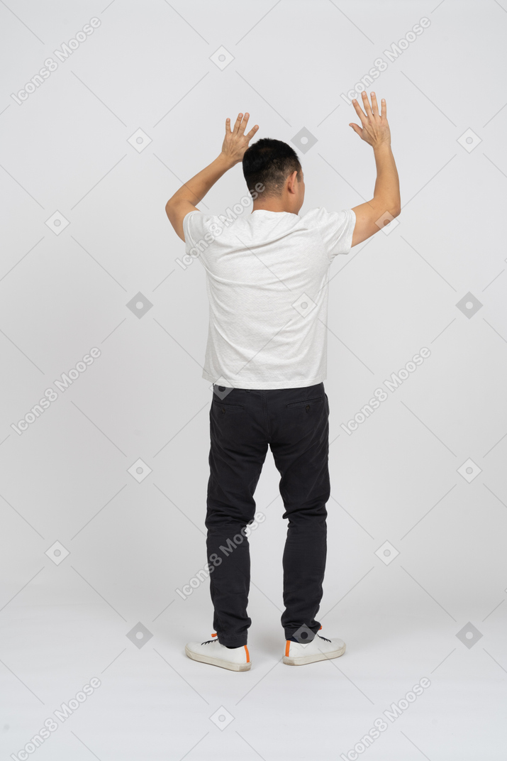 Rear view of a man in casual clothes standing with raised hands