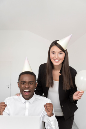 Man and woman wearing party hats behind desk in the office