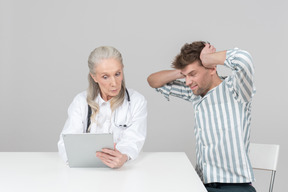 Aged female doctor showing something on her digital tablet to a patient