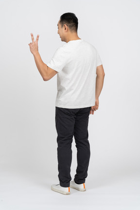 Three-quarter view of a man in casual clothes showing v sign