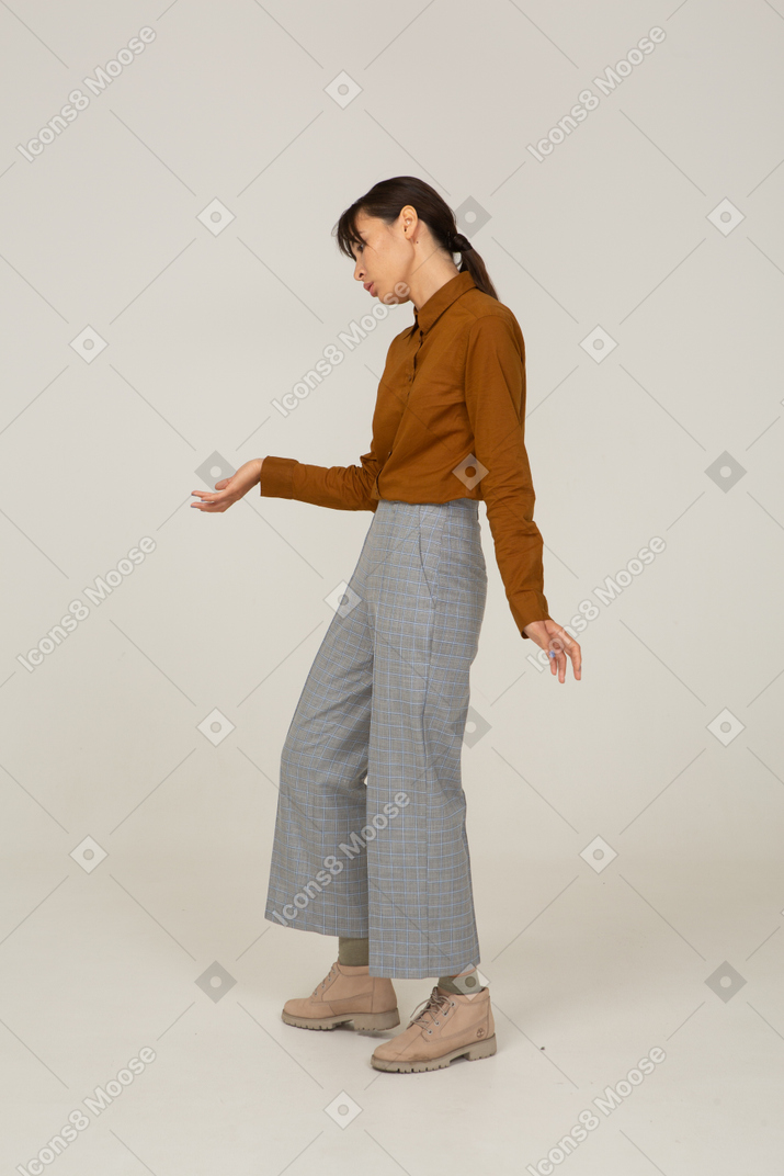Vista di tre quarti di una giovane donna asiatica in calzoni e camicetta che fa una riverenza