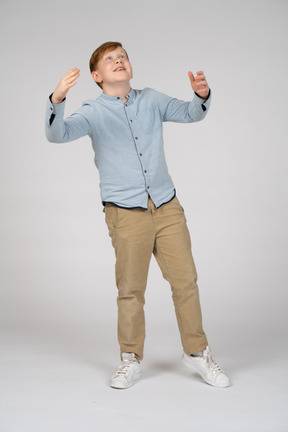 Front view of a happy boy standing with raised hands and looking up