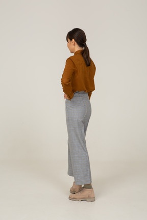 Three-quarter back view of a pouting young asian female in breeches and blouse putting hands on hips