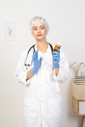 Front view of a young female doctor holding a jar of pills