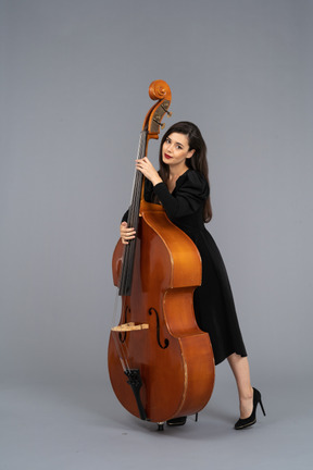Vista de tres cuartos de una joven músico en vestido negro sosteniendo su contrabajo