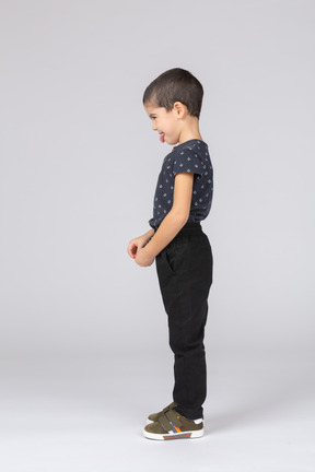 Вид сбоку милого мальчика в повседневной одежде, показывающего язык