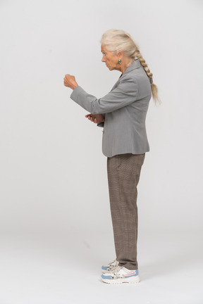 Vista laterale di una vecchia signora in abito che mostra il pugno