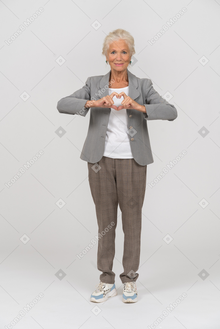 Vista frontale di una vecchia signora felice in abito che fa il segno del cuore con il dito