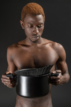 Close-up a young man holding a black saucepan with pasta in the dark