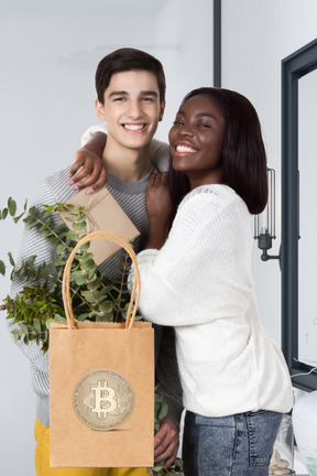 Interracial couple embracing while holding a bag with a bitcoin on it