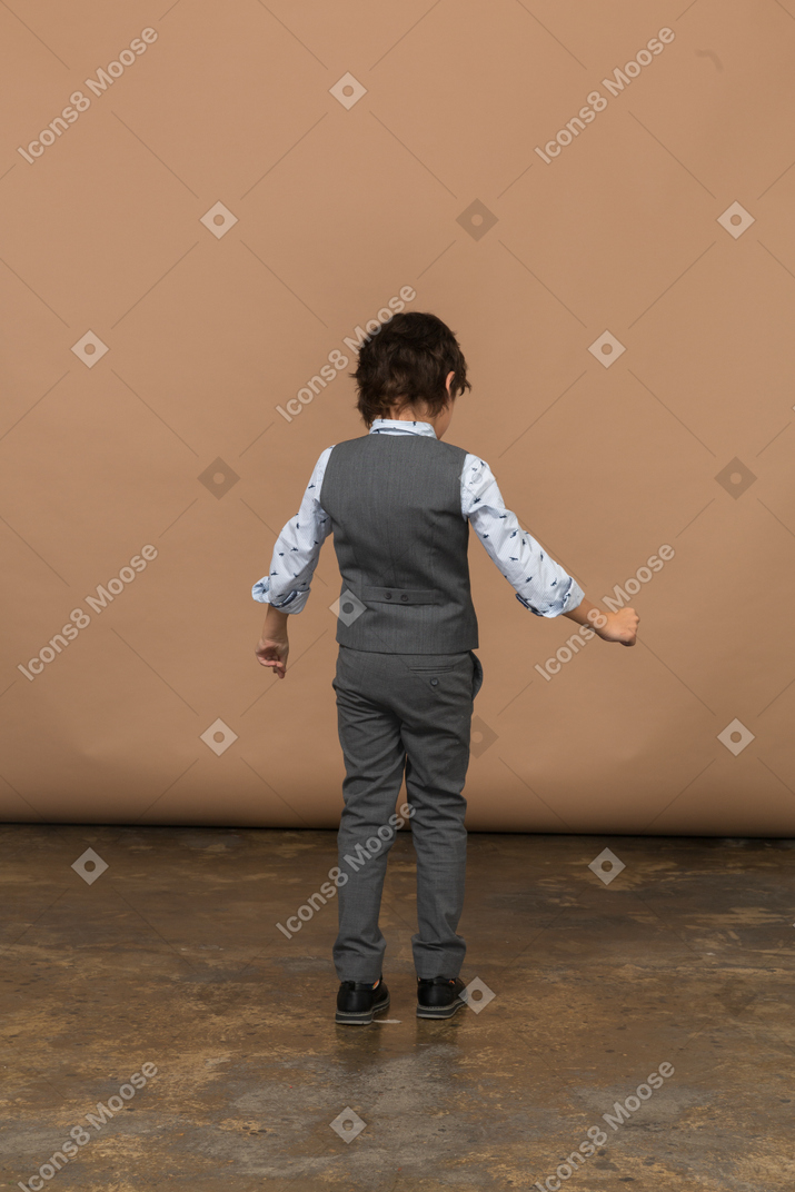 Vista traseira de um menino de terno em pé com os braços estendidos