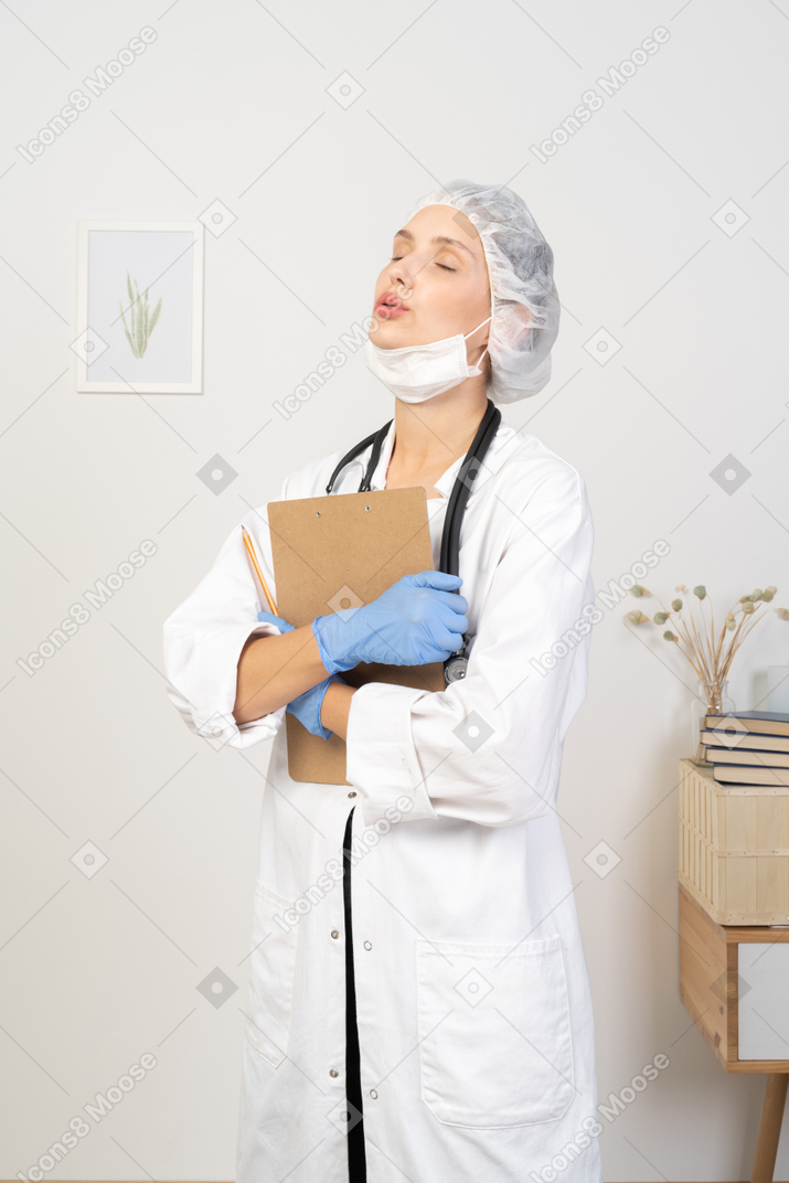 Vista de tres cuartos de una doctora joven soñolienta sosteniendo un lápiz y una tableta