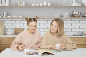 Two women sitting at a table and reading a magazine