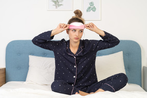 Vista frontal de una joven en pijama poniéndose máscara para dormir