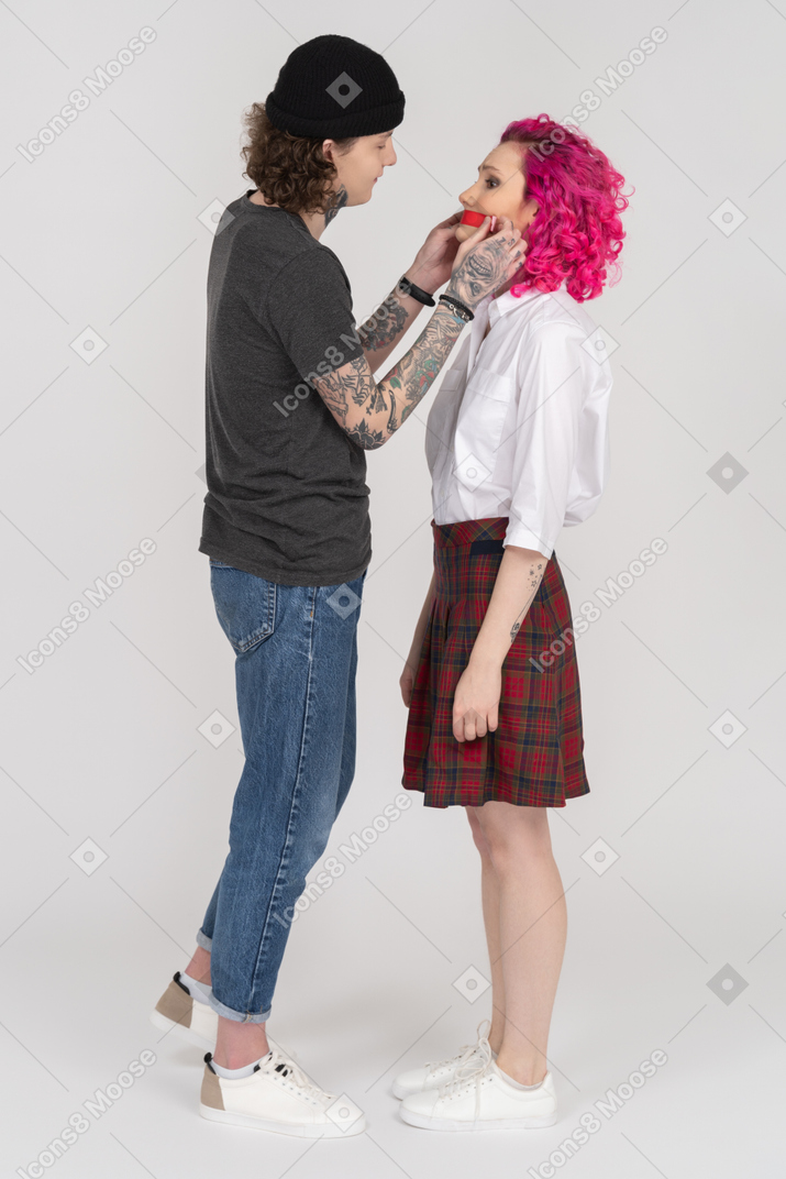 Side shot of a young male sticking red tape on his girlfriend's mouth