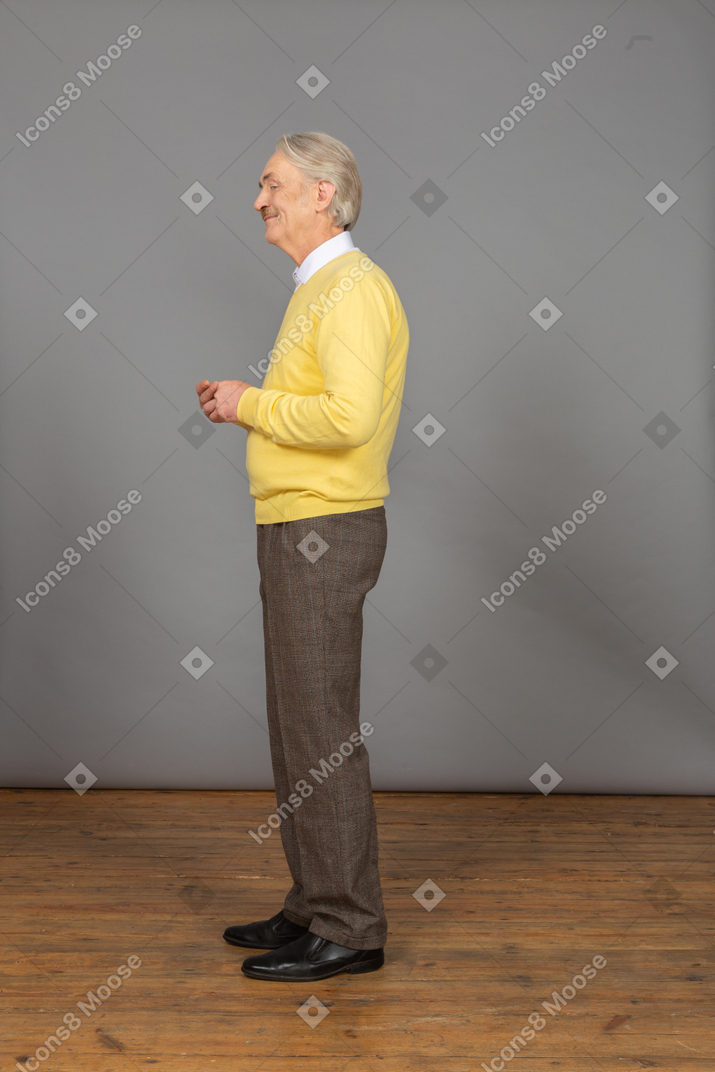 一个微笑的老人，穿着黄色套衫的侧视图，把手和他的眼睛一起闭着