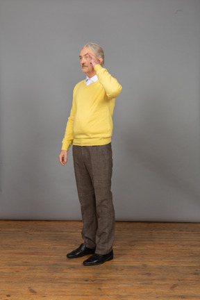 Three-quarter view of a confused old man touching head and wearing a yellow pullover