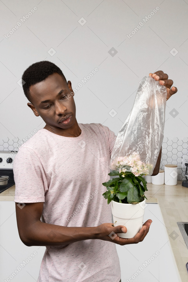 A man holding a plant in a plastic bag in the kitchen