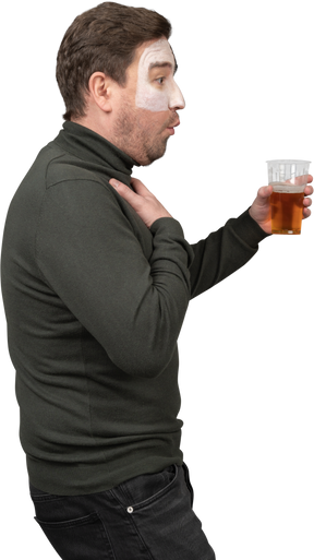 Vista lateral de un fanático del fútbol masculino sorprendido sosteniendo una cerveza