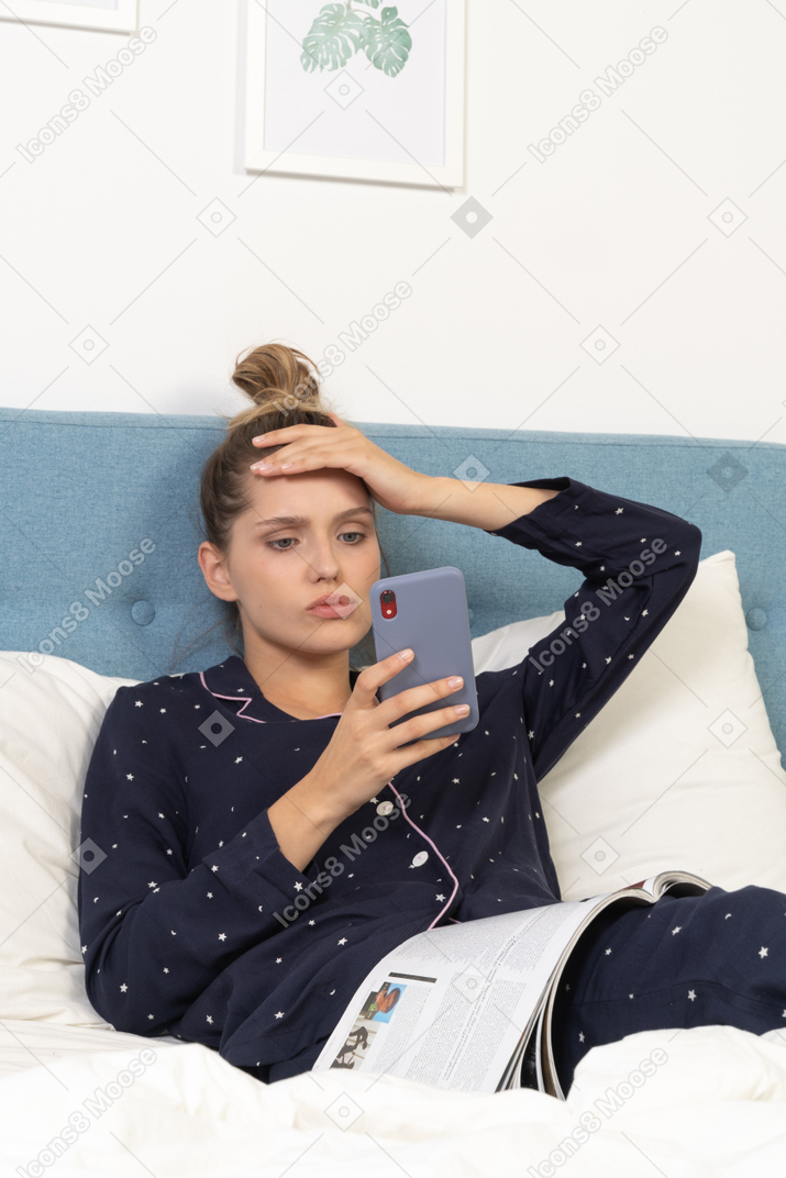 Primer plano de una mujer joven en pijama acostado en la cama mientras navega por la red