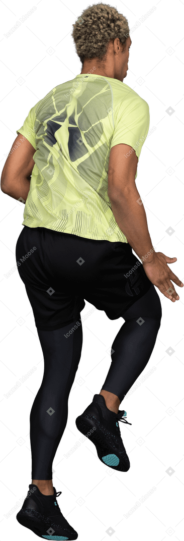 Трехчетвертный вид сзади прыгающего темнокожего молодого человека, поднимающего руку и сгибающего колени