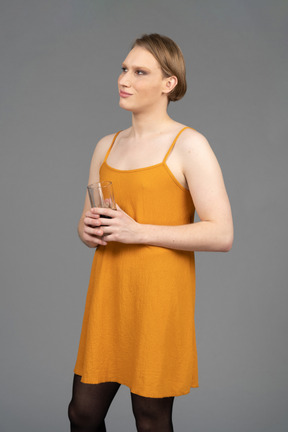 Giovane transgender in abito arancione con in mano un bicchiere