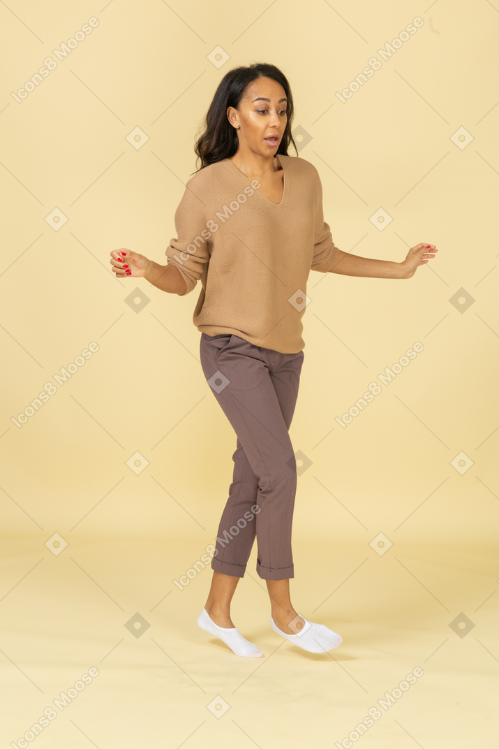 Vista de tres cuartos de una mujer joven asustada de piel oscura que camina extendiendo sus manos