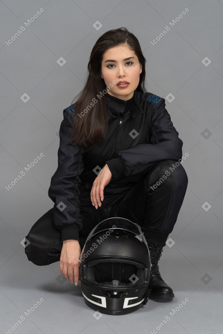 A beautiful young woman hunkering down next to a helmet