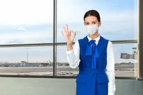 Flight attendant wearing face mask and showing ok gesture