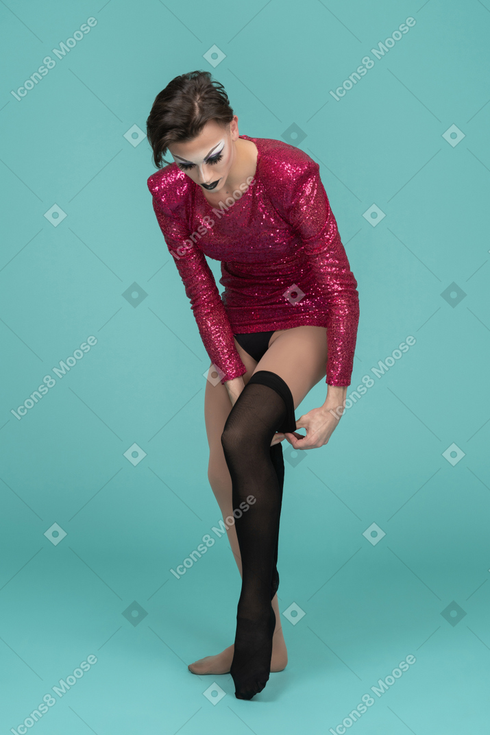 Трансвестит в розовом платье надевает черные носки до бедра