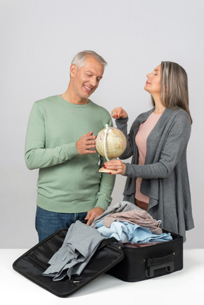 Middle aged couple holding globe while packing a suitcase