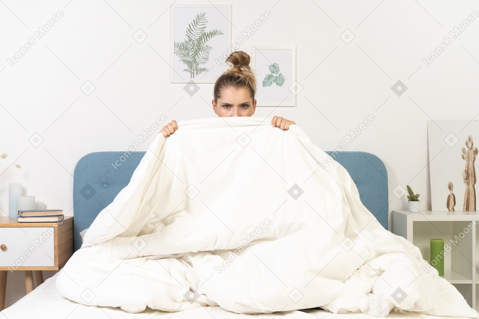 Front view of a young woman in pajamas hiding behind the blanket staying in bed