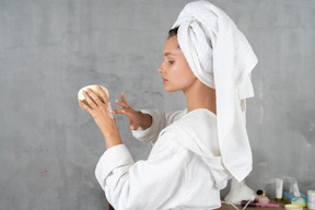 Vue latérale d'une femme en peignoir appliquant de la crème pour les mains