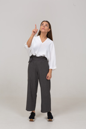 Vista frontal de una joven en ropa de oficina apuntando con el dedo hacia arriba