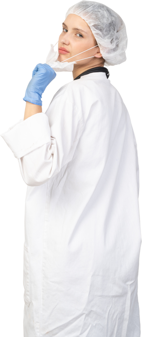 Vista posterior de tres cuartos de una joven doctora disgustada tratando de quitarse la máscara